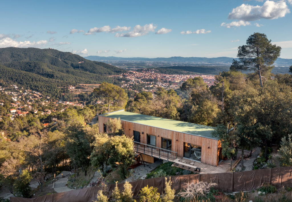 Vista aérea de una casa pasiva Eskimohaus. Se trata de una casa de una planta, alargada en medio de un entorno boscoso mediterráneo.