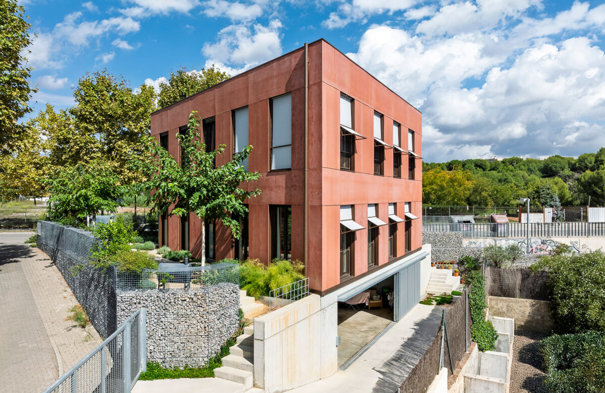 Casa unifamiliar de dos plantas con diseño Passivhaus, caracterizado por su fachada de viroc color terracota y ventanas grandes. La construcción de casa passiva en Sant Cugat incorpora elementos sostenibles y adornado de vegetación.