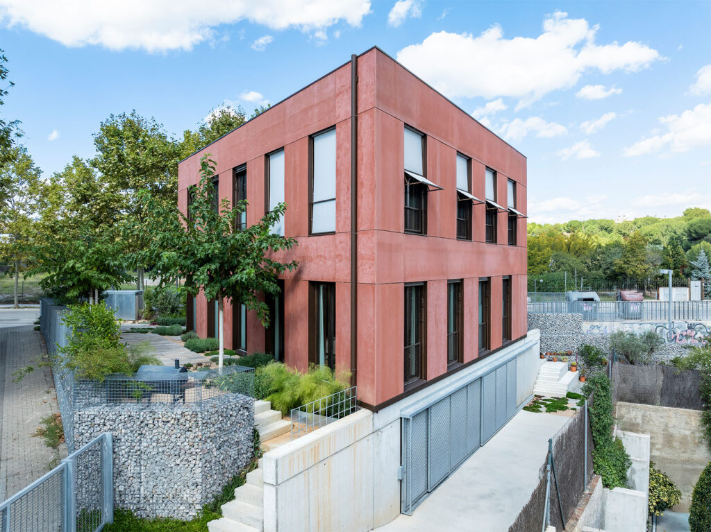 Construcció de casa passiva amb disseny de planta triangular i minimalista, finestres amb persianes i integració de vegetació al voltant. La construcció casa sostenible a Sant Cugat és un exemple de disseny eficiència energètica.