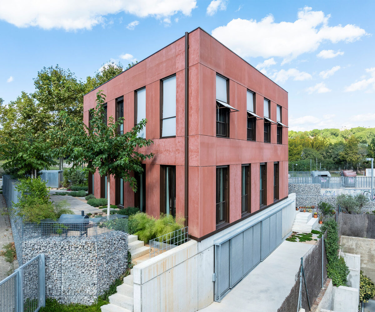 Construcció de casa passiva amb disseny de planta triangular i minimalista, finestres amb persianes i integració de vegetació al voltant. La construcció casa sostenible a Sant Cugat és un exemple de disseny eficiència energètica.